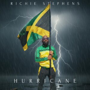 Album cover for Richie Stephens’ single Hurricane, showing Richie holding a large Jamaican flag in heavy rain and lightning with a dramatic storm backdrop